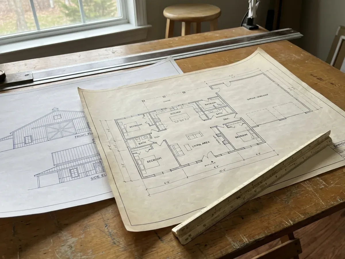 Barndominium floor plan and elevation drawings laid out on a drafting table with a scale rule.